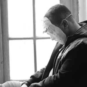 man in hoody with a white face mask sitting